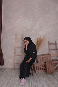 Full length of smiling woman in burka sitting on wooden chair