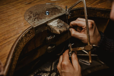 Goldsmith cutting metal with saw while making jewellery in workshop