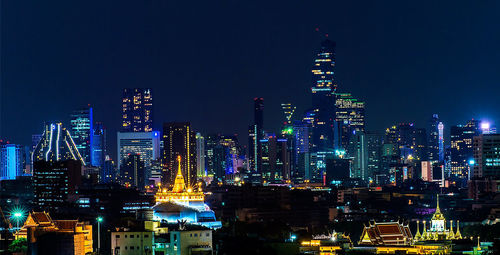 Illuminated modern buildings in city against sky at night