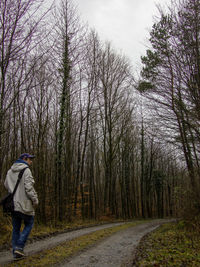 Man walking on road amidst bare trees in forest