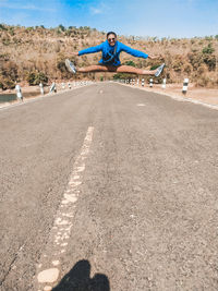 Man jumping in mid-air on road against trees