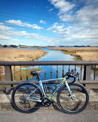 Bicycles on railing by lake against sky