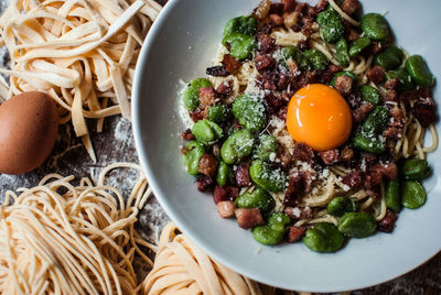 Close-up of vegetables with egg yolk in bowl by pasta on table