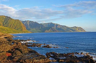 View of a calm ocean, rocky coastline and waianae mountain range at sunset on west oahu, hawaii.