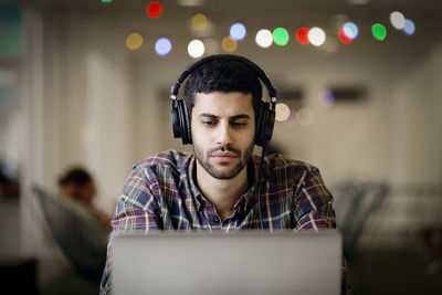 Businessman wearing headphones while working late on laptop in creative office