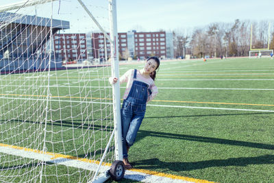 Playful woman standing by goal post on multi-purpose stadium
