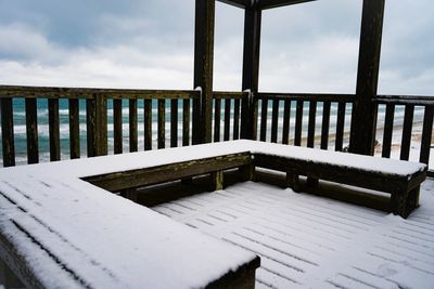 Empty bench by sea against sky