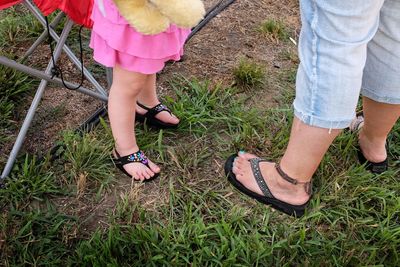 Low section of mother with daughter standing on grassy field