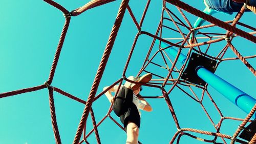 Low angle view of woman climbing on ropes at playground against clear sky