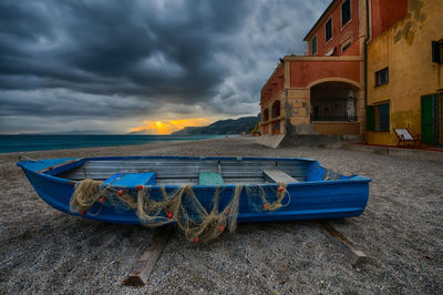 Boats moored on beach by buildings against sky