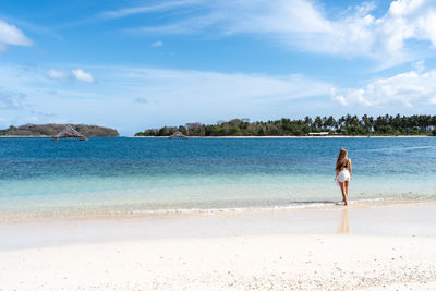 Rear view of woman standing at beach against sky