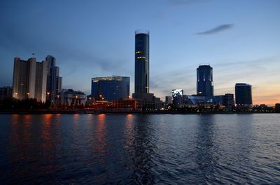 River by buildings against sky in city during sunset