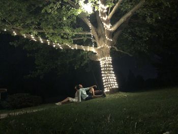 People sitting on field by trees at night