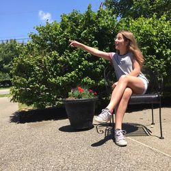 Smiling woman pointing while sitting on chair against plants