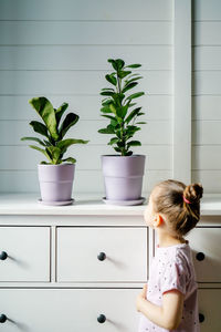 The girl looks at the two lavender pots on the dresser.