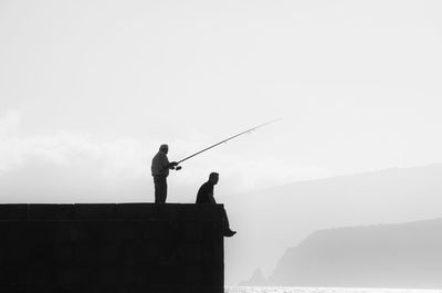 Silhouette man fishing on mountain against sky