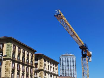 Low angle view of crane by building against clear blue sky