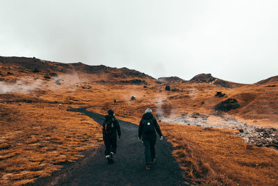 Rear view of people walking on mountain against sky