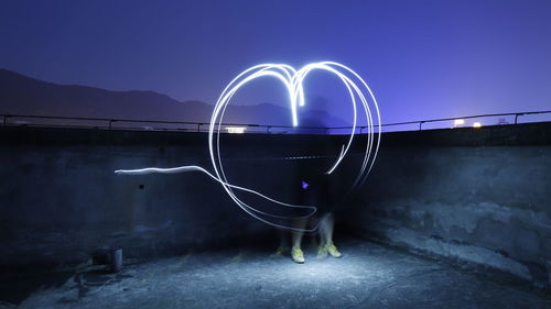 Rear view of person standing on illuminated lamp at night