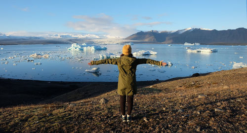 Rear view of woman with arms outstretched standing by frozen lake