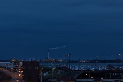 Illuminated factory in city against sky at night