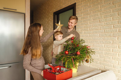 Family decorating the christmas tree against wall