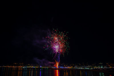 Firework display over illuminated city against sky at night