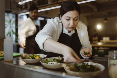 Focused female chef garnishing salad with cilantro in commercial kitchen