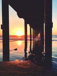 Silhouette bridge over sea against sky during sunset