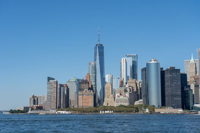 Buildings by river against clear blue sky