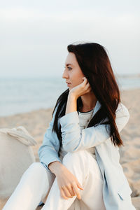 Young woman sitting on shore at beach against sky