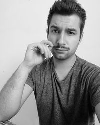 Portrait of young man touching mustache against wall