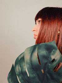 Beautiful young woman holding leaf against white background