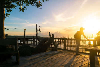 Full length of man looking at sea while standing on pier against sky during sunset