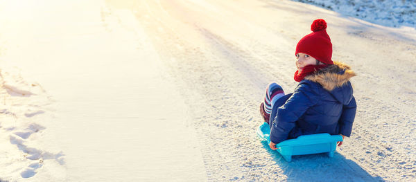 Cute girl in warm clothing sledding on snow