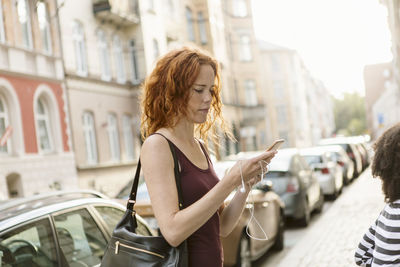 Woman using mobile phone on sidewalk in city