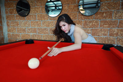 Young woman playing with umbrella on table against wall