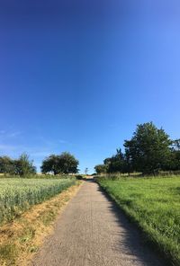 Road amidst field against clear blue sky