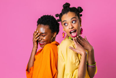 Portrait of young woman standing against pink background