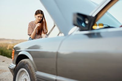 Side view of young woman sitting on car