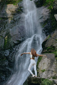 Rear view of woman standing against waterfall