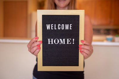 Midsection of woman holding sign at home