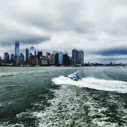 View of city at waterfront against cloudy sky