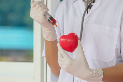 Midsection of doctor holding syringe over red heart shape