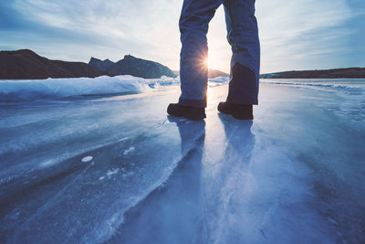 Low section of man standing on frozen land against sky during winter