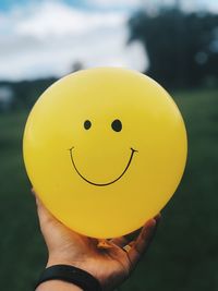 Close-up of hand holding yellow balloon with anthropomorphic face