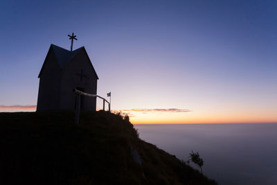 Silhouette building by sea against sky during sunset