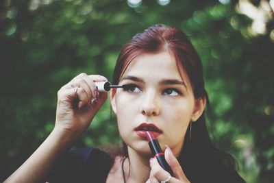 Close-up of young woman looking up while applying makeup on face