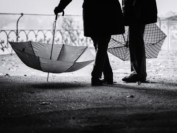 Low section of silhouette friends with umbrellas standing on field