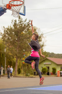 Young woman with short hair in sportswear playing basketball on the street